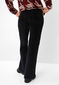 Zwarte fluwelen flared broek met achterzakken, met een verticale ribbelstructuur. Gedirigeerd met een gestreepte lange mouwtop en stevige laarzen.