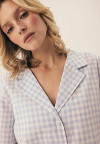 Jasnoniebieska bluzka w białą kratkę z kołnierzykiem i zapięciem na guziki, charakteryzująca się miękką teksturą materiału oraz luźnym krojem.