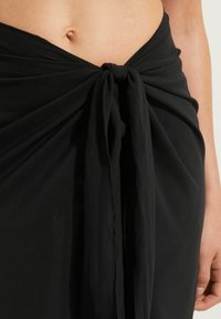 Jupe noire enroulée avec un détail de nœud à la taille, fabriquée en tissu léger et doux, présentant une texture lisse et un design fluide.