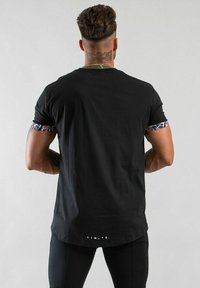 Svart t-shirt med blomstermönstrade ärmar, rund hals och längre bakstycke. Textdetalj i botten säger "LIM.Y.E."