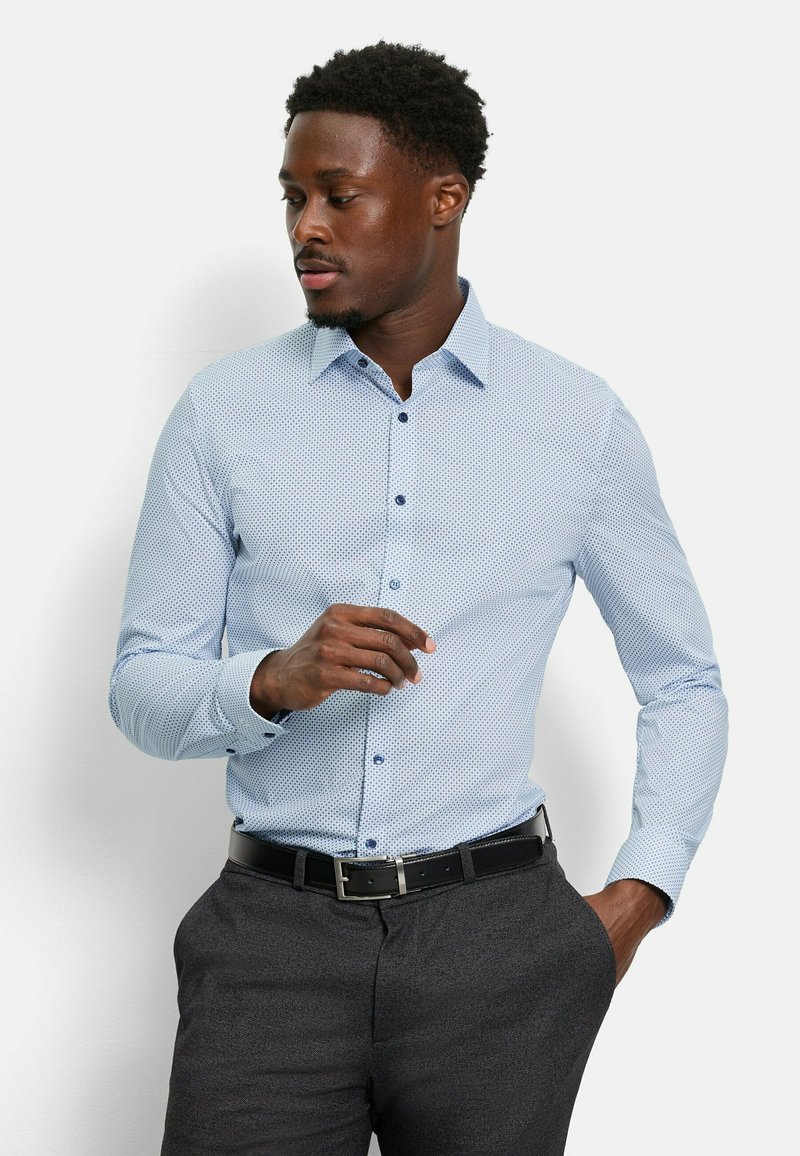 Hellblau gemustertes Hemd mit kleinen Punkten, langen Ärmeln, Button-Down-Kragen und dunklen Knöpfen, kombiniert mit dunkelgrauen Hose und einem schwarzen Gürtel.