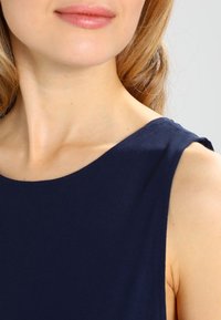 Sotilas sininen hihaton paita, jossa on sileä pinta ja pyöreä pääntie, esittellen yksinkertaista muotoilua ilman lisäkuvioita tai koristeita.