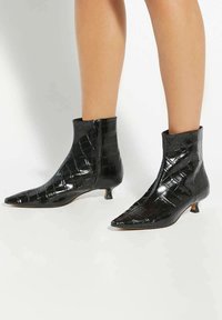 Black ankle boots with a crocodile pattern, pointed toe, and a short kitten heel. Made of glossy material, featuring a side zipper.