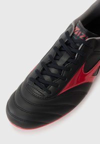 Black leather sneaker featuring a red glossy accent, flat laces, and textured surface with visible stitching on a light background.