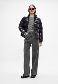 Melnas pūkainās virsjakas ar spīdīgu apdari, svītrainas garās piedurknes krekls un pelēkas augsta josta platās bikses, apvienotas ar melnajām zābakām.