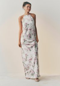 Lang, halterneck kjole lavet af glat stof, med en hvid baggrund og blomster mønstre i pink og grønne nuancer.