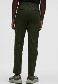 Rohelised püksid, mis on valmistatud kergest kangast, omavad kitsast lõiget, kahte tagumist taskut ja on ühendatud pruunide ja roheliste tossudega.