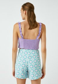 Top corto lilla con spalline arricciate e schiena smock, abbinato a pantaloni corti a vita alta con un motivo floreale dai colori pastello su una base chiara.