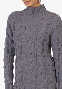Maglione grigio lavorato a maglia con un alto collo a coste, caratterizzato da un motivo a treccia testurizzato su tutta la superficie e polsini a coste sulle maniche.
