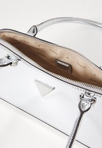 Zilveren patenten leren handtas met ritsluiting. Interieur met beige voering en herhaald merklijn, plus een klein zakje. Dubbele handvatten.