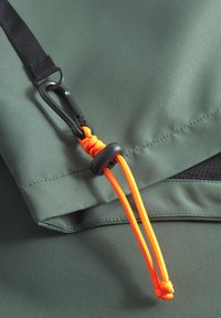 Groene stof met een matte afwerking heeft een oranje verstelbaar trekkoord en een zwarte karabijnhaak die aan een naad is bevestigd.