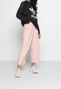Svart långärmad tröja med vit Adidas-logotyp, matchad med cropped rosa byxor och vita sneakers. Tröjan har strukturerade ränder på ärmarna.