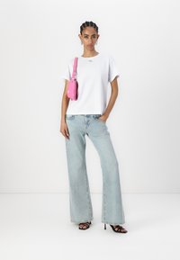 Tricou alb cu mânecă scurtă și logo, blugi deschiși la culoare cu talie înaltă și evazați, geantă roz și sandale negre cu toc; material neted, croi lejer.
