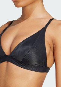 Svart ribbad bikiniöverdel med triangulära kupor, smala band och en mjuk lyster. Har märkesdetaljer längs bandet.