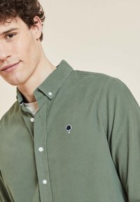 Groene corduroy overhemd met knopen, voorzien van een geborduurd boomembleem op de borst, met een ontspannen pasvorm en subtiele textuur.