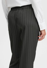 Zwarte pinstripe broek met een elastische tailleband en een gladde textuur. Bevat smalle witte strepen die verticaal over de stof lopen.