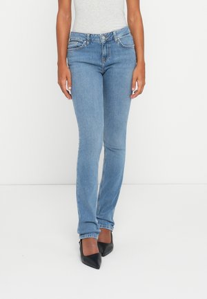 Light blue denim jeans with a slim fit, subtle stitching details, and a classic five-pocket design, paired with black pointed-toe heels.