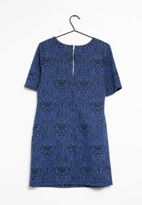 Kortärmad blå klänning med ett svart utsmyckat mönster, rund halsringning och en synlig dragkedja bak. Hänger från ett svart hänge.