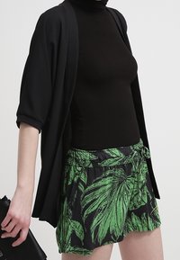 Černý žebrovaný rolák spárovaný s šortkami s potiskem zeleného listí. Oblečení doplňuje černý oversized kimono a černá kabelka.