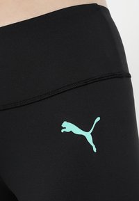 Leggings sportivi neri con una texture liscia, caratterizzati da un logo Puma azzurro chiaro sul lato sinistro. Design semplice e aderente.
