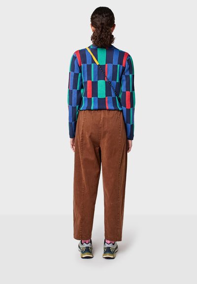 Suéter de cuadros multicolor en azul, verde y rojo; combinado con pantalones de pana marrones y zapatillas deportivas negras y amarillas.