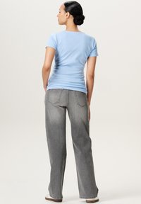 Lys blå, kortærmet skjorte parret med løse, grå jeans. Stoffet ser glat ud, med et simpelt design og uden synlige mønstre.