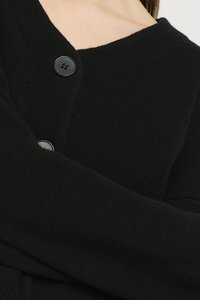 Cardigã preto feito de um tecido de malha texturizado, com decote em V e um único botão preto como detalhe perto do colarinho.