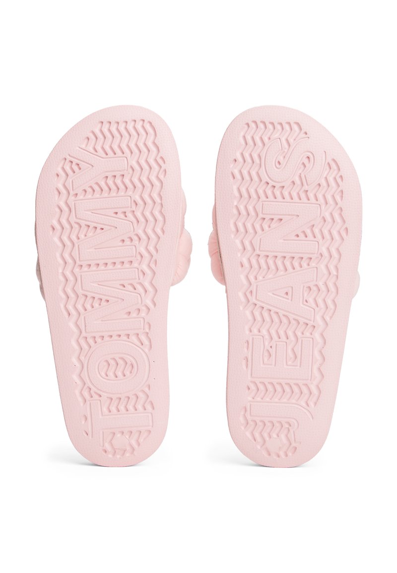 Rosa Gummi-Flip-Flop-Sohlen mit strukturierten Mustern. Das Wort "TOMMY" ist auf der linken Sohle erhaben, und "JEANS" ist auf der rechten Sohle erhaben.
