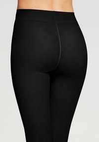 Svarta ribbade leggings med bred midja och slät textur, designade för att forma kroppen med minimala sömmar för en strömlinjeformad look.