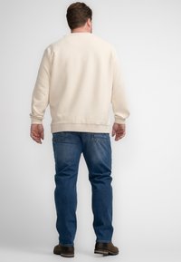 Crème-kleurige sweatshirt met geribde boorden en halslijn, gecombineerd met blauwe jeans, voorzien van zichtbare achterzakken en een rechte pijp.