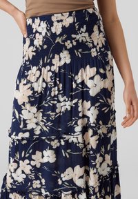 Kvinna som bär en mörkblå kjol med vitt och ljust rosa blommönster, elastisk midja och flerlagrade volanger, ihop med en brun topp.