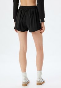 Pantalones cortos deportivos negros con una cintura elástica, que presentan un ajuste suelto y una textura suave. Se llevan con calcetines blancos y zapatos casuales.