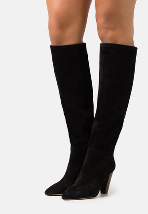 Bottes hautes en daim noir, dépassant le genou, avec un bout pointu et un talon empilé. Le design présente une texture lisse et une silhouette ajustée.