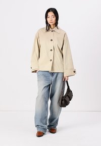 Beige, overdimensjonert jakke med store knapper, parret med lyseblå, løstsittende jeans og brune sko. Holder en mørk skulderveske.
