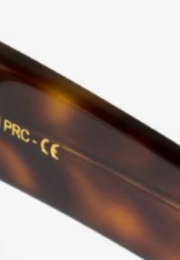 Montatura di occhiali in acetato tartarugato con superficie liscia, dotata di testo dorato che indica l'origine e la certificazione.