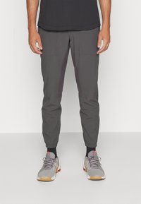 Szare spodnie sportowe z elastycznymi mankietami, kieszeniami z przodu i kontrastowymi panelami bocznymi. Noszone z szarymi trampkami i czarnymi skarpetami.