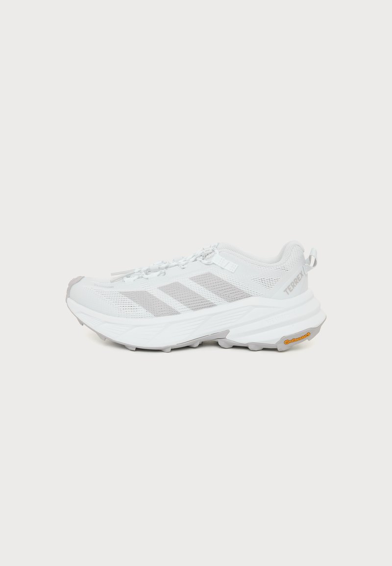 Chaussure de trail running Adidas Terrex blanche avec des bandes grises et une semelle texturée, montrée de profil sur un fond uni.