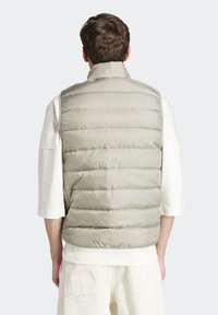 Světlezelená prošívaná vesta s horizontálním prošitím, vysokým límcem a hladkým povrchem, nošená přes bílé triko s dlouhým rukávem.