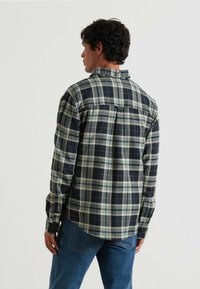 Camisa de cuadros con una combinación de colores en azul marino oscuro y verde, de manga larga y con dobladillo curvado. Fabricada en tejido tejido con cuello abotonado.