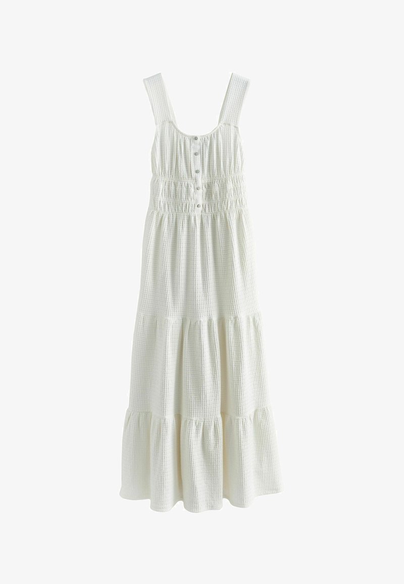 Robe maxi blanche sans manches avec larges bretelles, corsage à boutons sur le devant, taille élastiquée smockée, et jupe à volants superposés en tissu texturé.