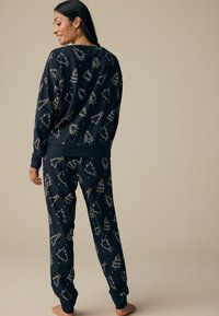 Marineblå pyjamas-sæt med hvide og gyldne juletræsmønstre. Fremstillet af blødt stof, inkluderer en langærmet bluse og bukser med elastisk talje.