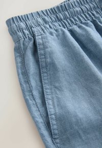 Shorts en coton bleu clair, avec taille élastique, poches latérales, texture lisse et détails de couture subtils. Vue rapprochée de la taille et du tissu.