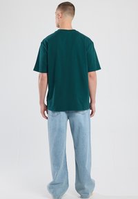 Vihreä puuvillapaita lyhyillä hihoilla, rento mitoitus ja pyöreä kaula-aukko, yhdistettynä vaaleansinisiin leveälahkeisiin farkkuihin. Yksinkertainen muotoilu, ei kuvioita.