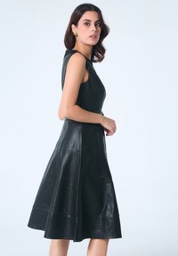 Robe en cuir noir de forme A avec un corsage ajusté et une jupe évasée. Présente une texture lisse et un design sans manches.