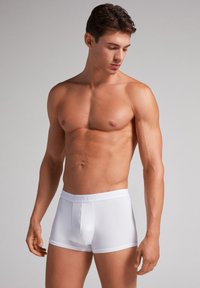 Hvide boxer shorts med en glat tekstur, tætsiddende design og en blød elastisk talje med subtil branding. Minimalistisk stil og ensfarvet.