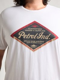 Bílý bavlněný tričko s velkým červeným a černým grafickým motivem ve tvaru diamantu, na kterém je nápis "Petrol Ind." a textové detaily ve vintage stylu.