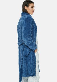 Blauwe pluche badjas met een diamantgestikte textuur, lange mouwen en een zelfbindende riem. Gekozen over lichte, gestreepte pyjama's.