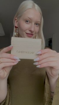 Valentino kaarditasku beežist nahast, millel on kullatud logo, õhuke ristkülikukujuline kuju ja mitmed kaardipesad. Sile tekstuur puhaste joontega.