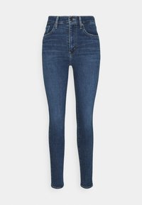 Sötétkék denim anyagból készült skinny farmernadrág. Magas derekú, sima textúrával, öt zsebével és elülső gombos záródással.