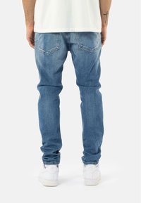 Jeans de denim de color azul claro con un corte recto, que presentan bolsillos traseros y detalles de desgaste, combinados con zapatillas blancas.